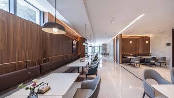 A modern restaurant with long communal tables and booths, wooden paneling, and a marble floor.