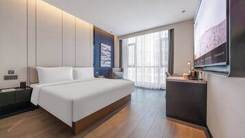 A modern hotel room with a large bed, a desk, and a television.