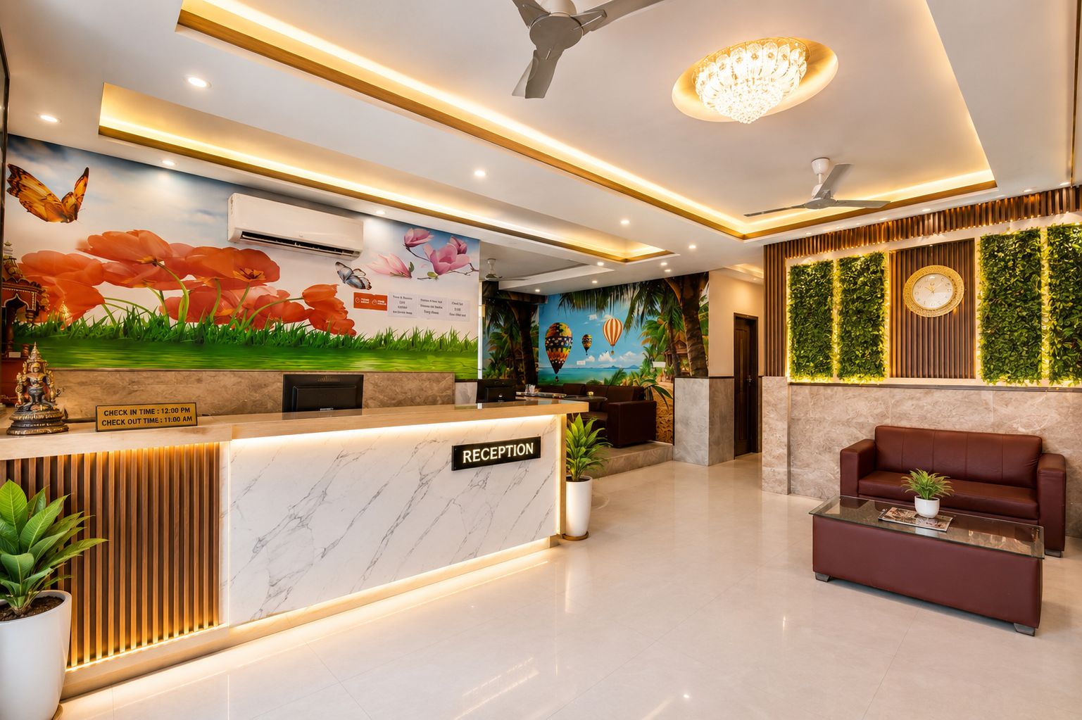 Uma área de recepção com balcão de mármore, um candelabro e um mural com flores e uma cena de praia.