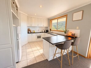 Uma cozinha moderna com armários brancos, uma ilha com bancada preta e dois banquetes.