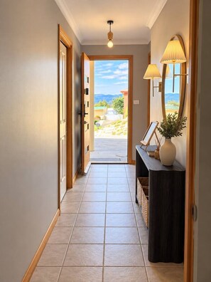 A hallway with a view to the outside, a door, a console table with a lamp, and a vase. - Wallcrest Retreat | 5BR, Views, Pets & Parking (Berriedale)