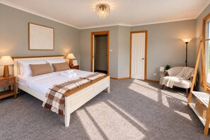 Ein Schlafzimmer mit einem Bett, Nachttischlampen, einem Sessel und einer Tür.