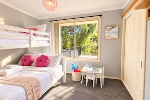 Quarto com beliches, escrivaninha e janela com vista para árvores.