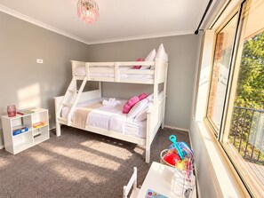 A bunk bed with a white frame, a small white nightstand, and a window with a view of greenery. - Wallcrest Retreat | 5BR, Views, Pets & Parking (Berriedale)