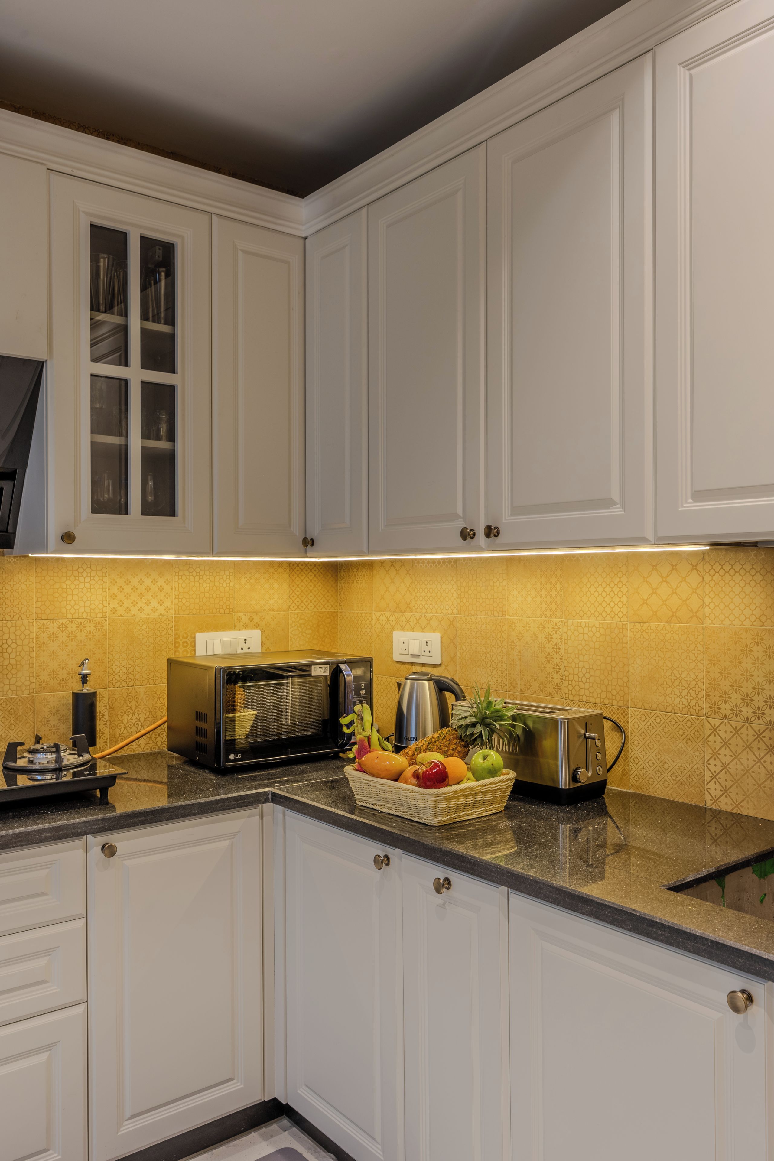 A kitchen with white cabinets, a microwave, a kettle, and a fruit basket on the counter.