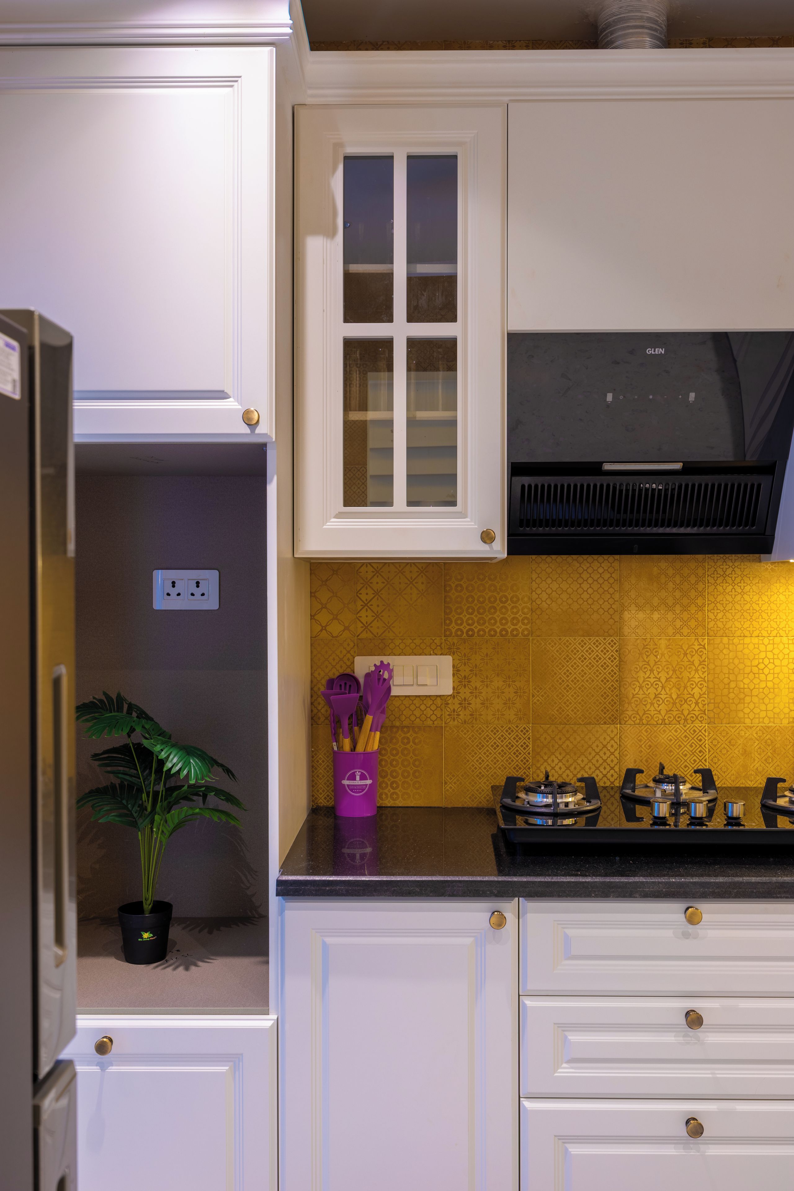 A kitchen with white cabinetry, a black range hood, and a yellow patterned backsplash.