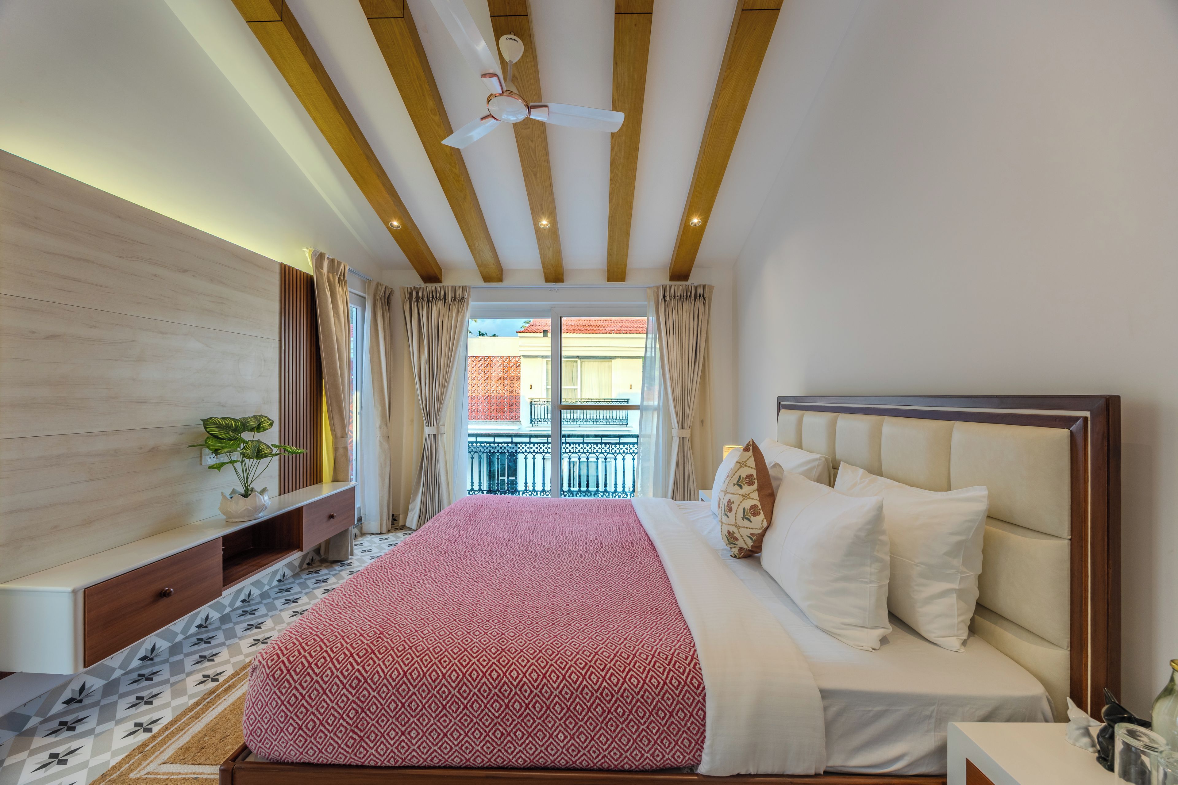 A bedroom with a bed, a bedside table, a nightstand, a ceiling fan, and a view of the outside.
