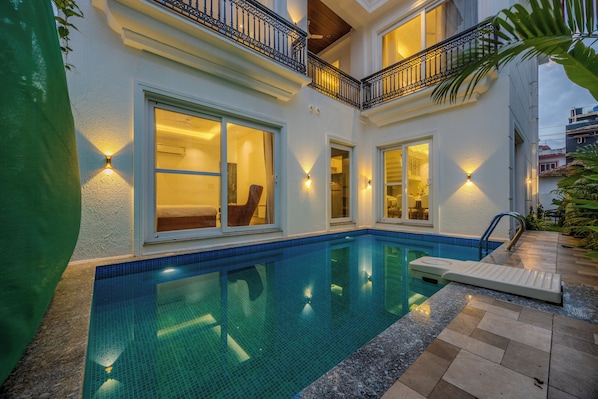 A residential building with a swimming pool, large windows, and outdoor lighting.