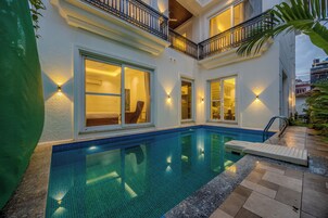 A residential building with a swimming pool, large windows, and outdoor lighting.