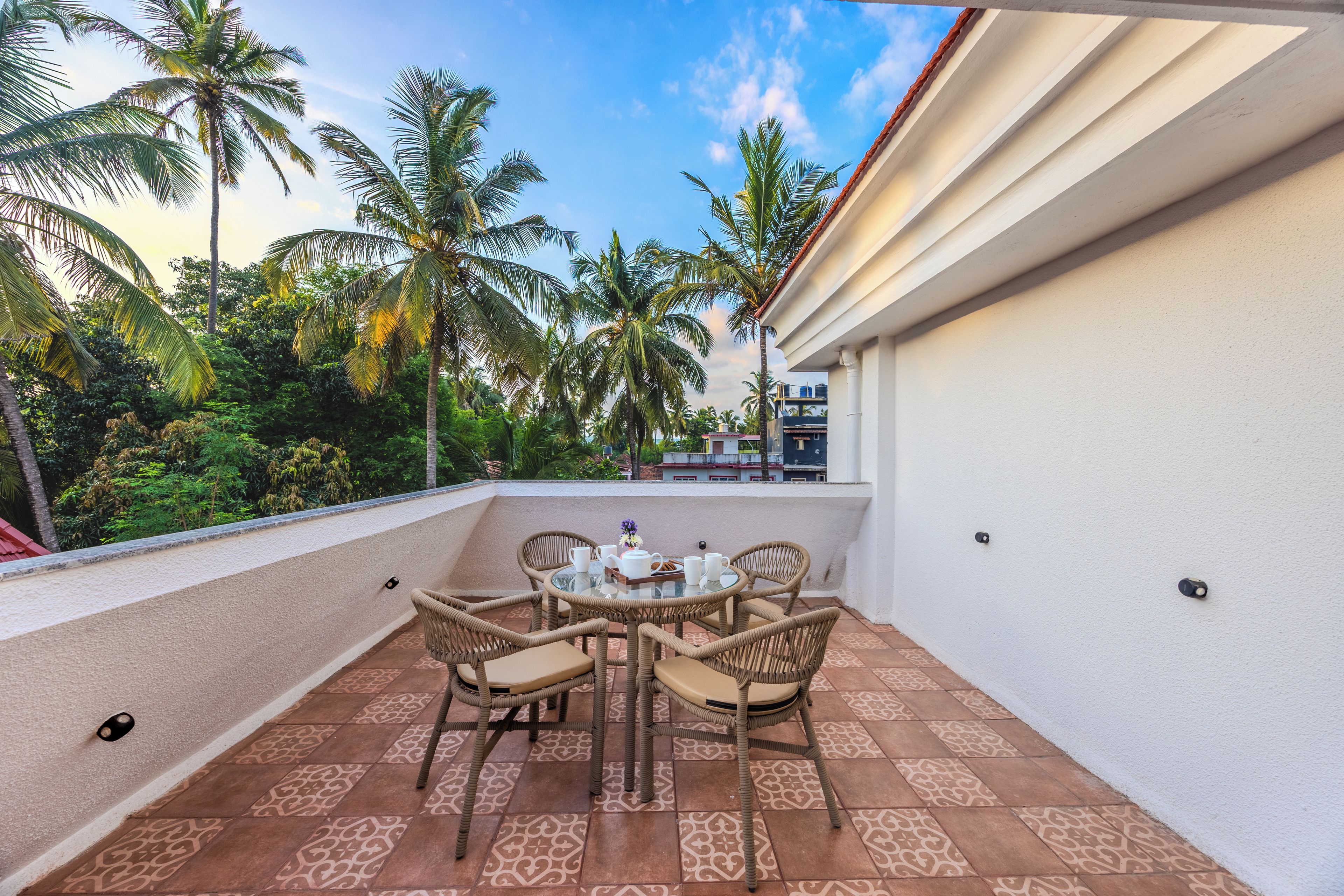 A balcony with a table and chairs, surrounded by palm trees and a clear sky.