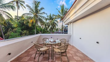 A balcony with a table and chairs, surrounded by palm trees and a clear sky.