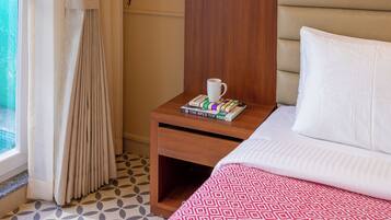 A hotel room with a bed, a nightstand, a lamp, a window with curtains, and a view of the outdoors.