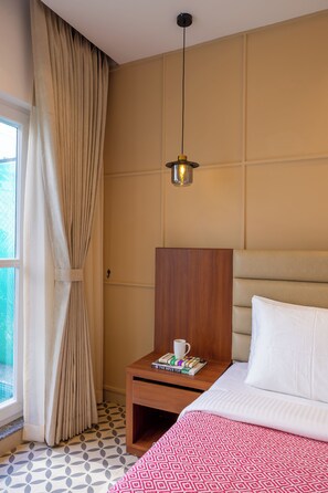 Quarto de hotel com cama, mesa de cabeceira, luminária, janela com cortinas e vista para o exterior.