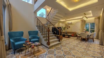 A spacious living area with a staircase, blue armchairs, a dining set, and patterned flooring.