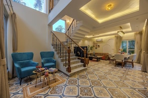 Een ruime woonkamer met een trap, blauwe fauteuils, een eethoek en vloerbedekking met een patroon.