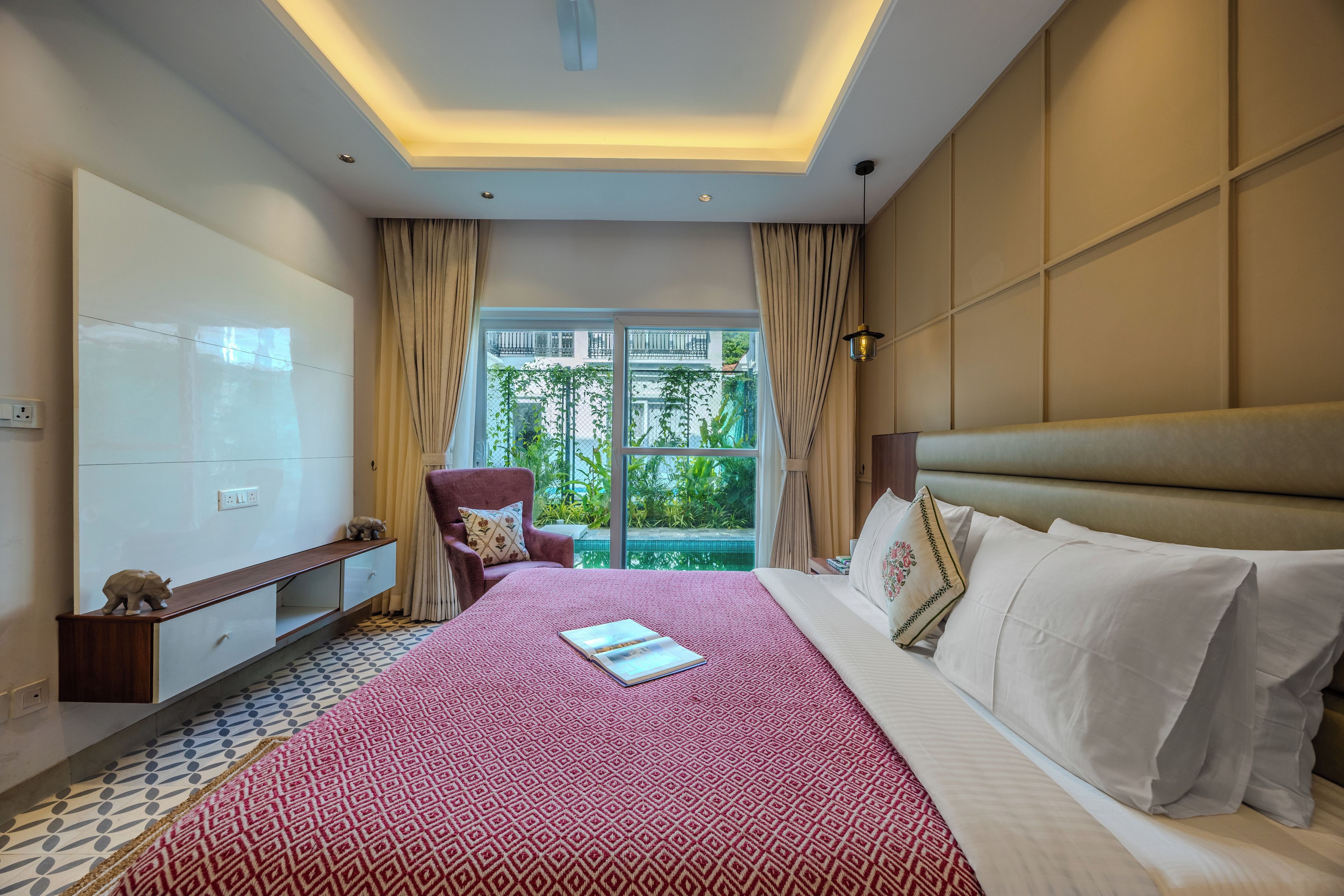 Habitación de hotel con una cama grande, una silla, un escritorio y vistas al exterior con vegetación.