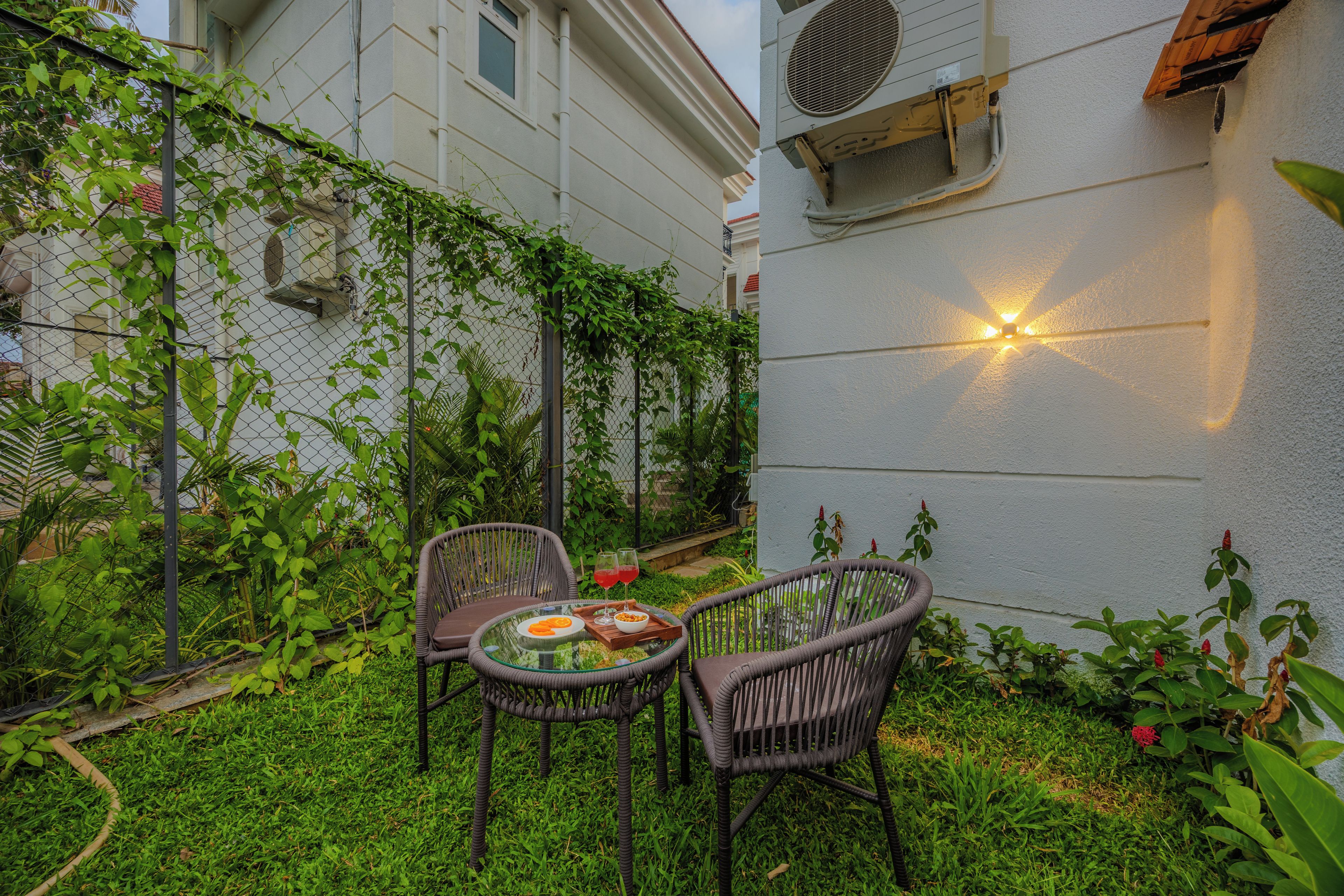 A patio with two wicker chairs, a glass table, and a small garden area with plants and a fence.