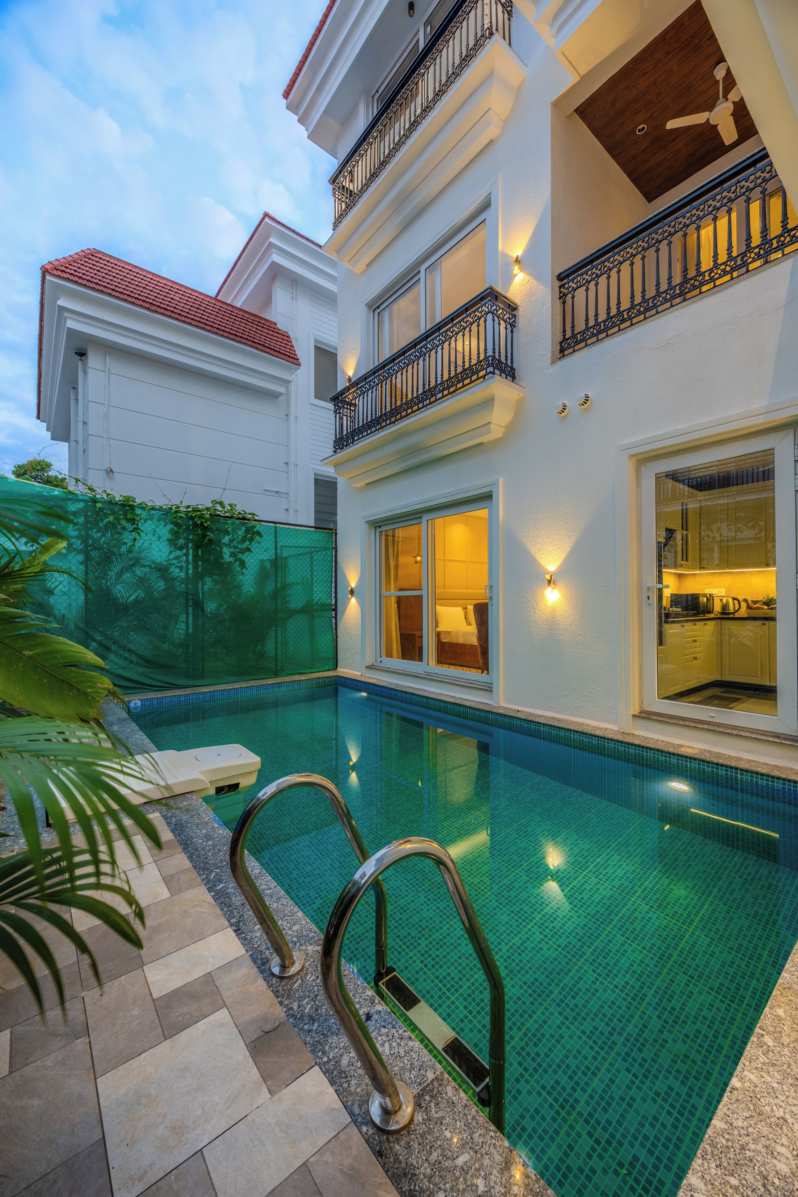 A two-story building with a swimming pool, a covered patio, and a visible kitchen area.