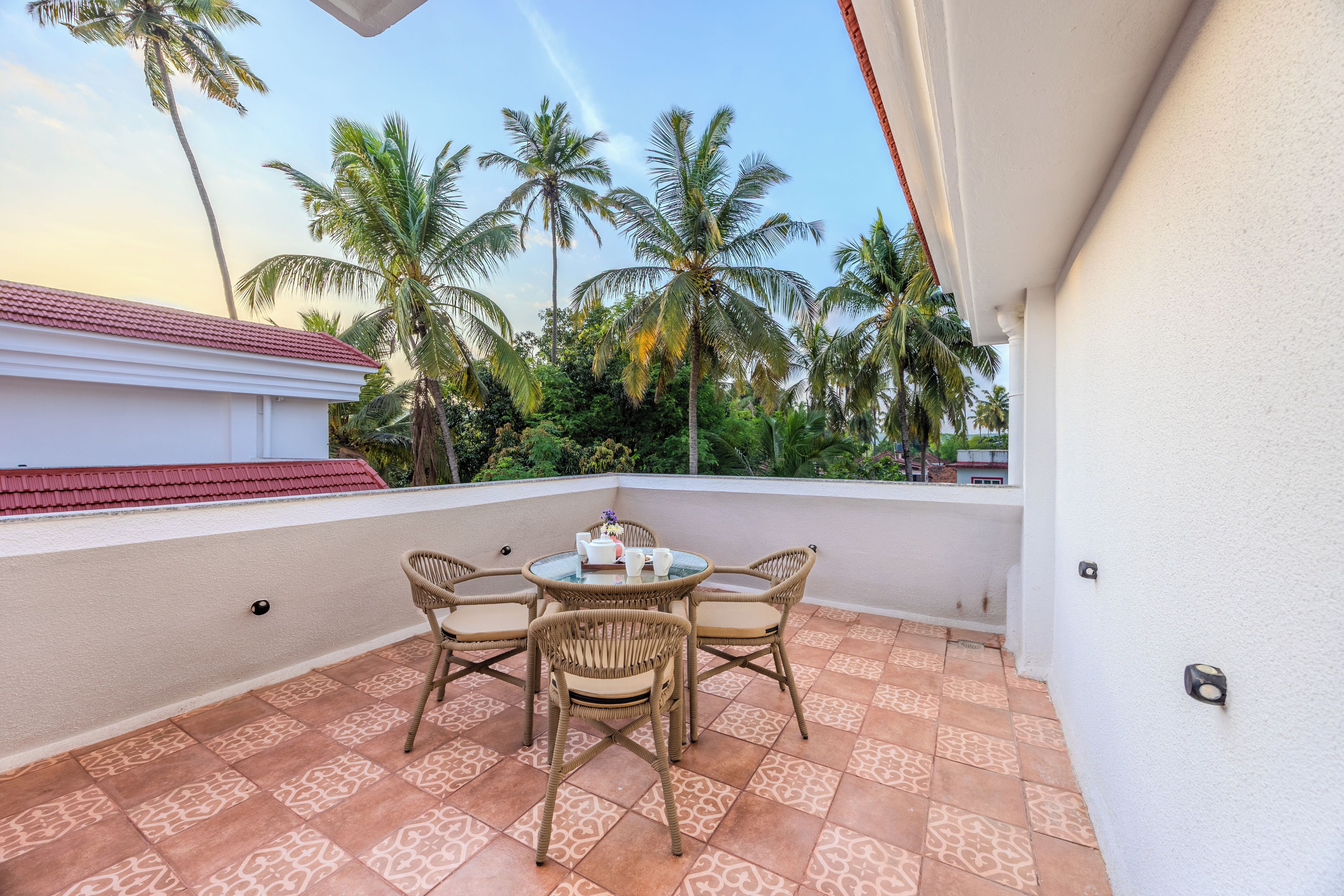 A balcony with a round table and wicker chairs, surrounded by patterned tiles.
