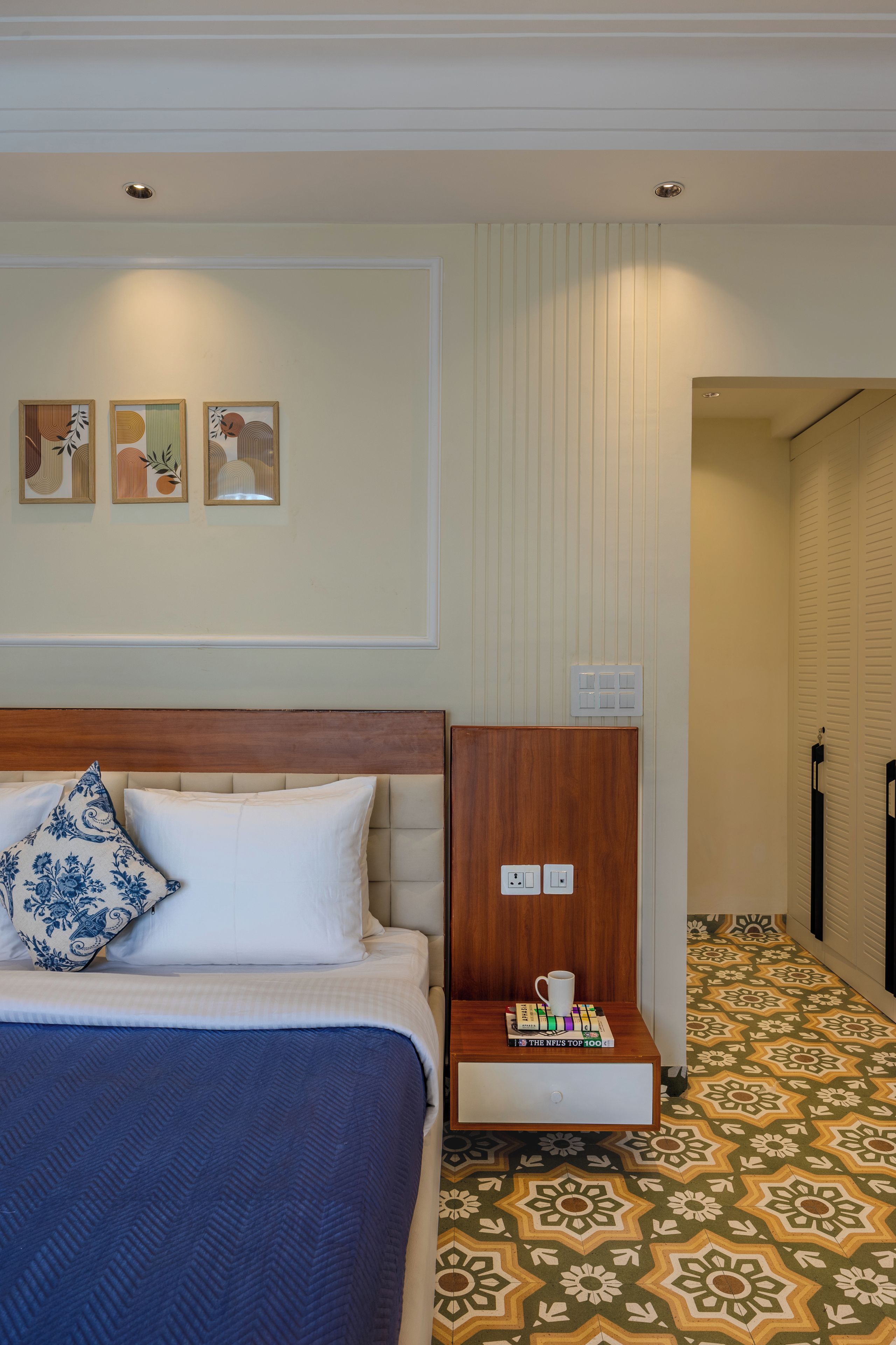 A hotel room with a bed, a nightstand, and a wall with three framed pictures.