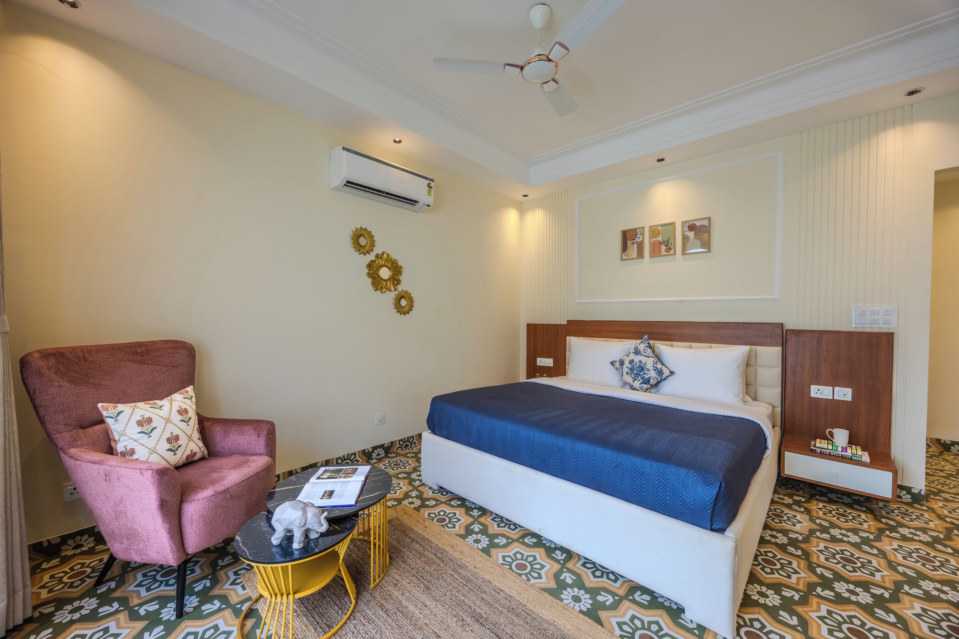 A hotel room with a bed, a chair, a small table, an air conditioning unit, and a ceiling fan.