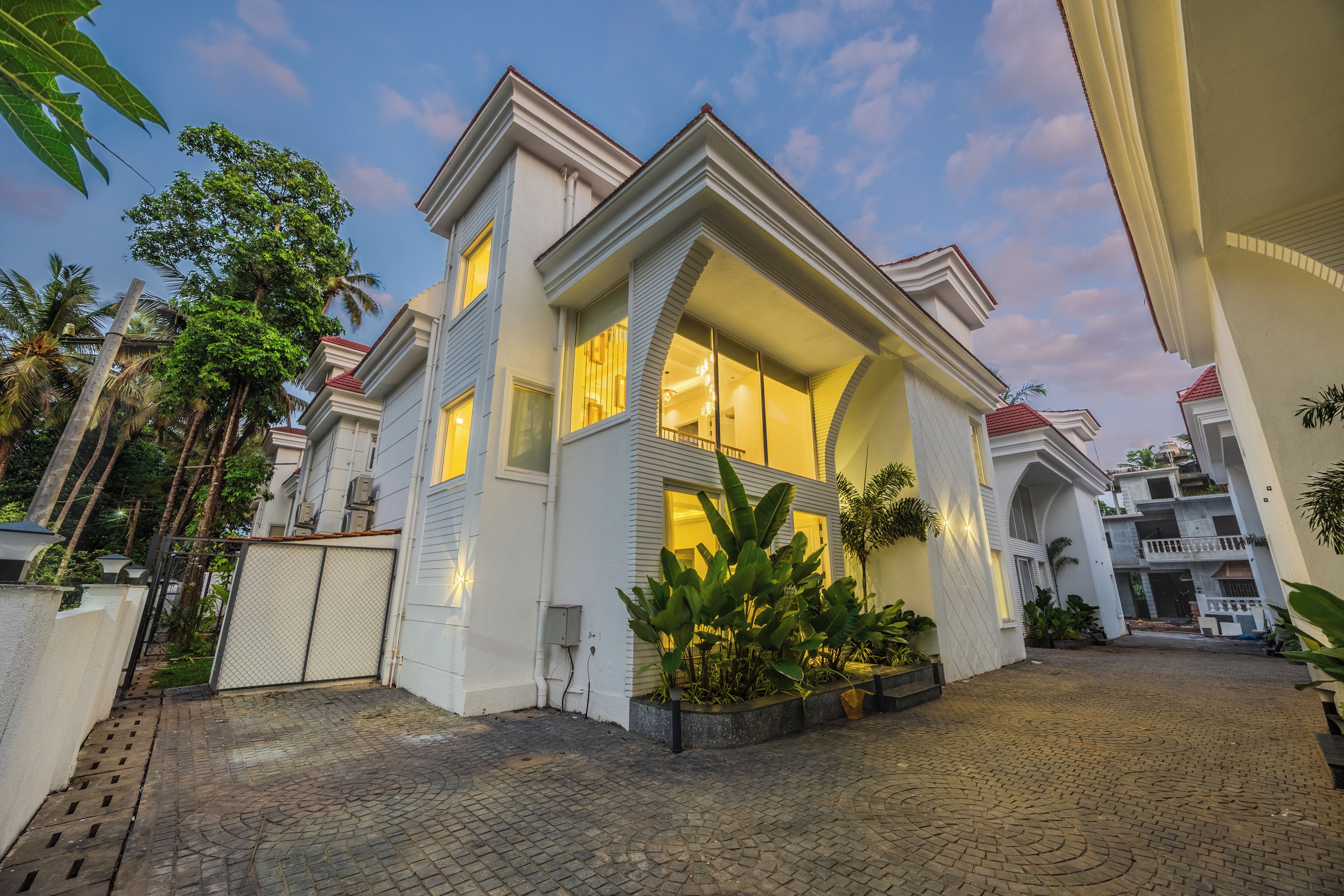 A modern two-story house with a large bay window, a gated entrance, and a paved driveway.