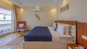A hotel room with a bed, a chair, a small table, an air conditioning unit, and a window with a view of a building.