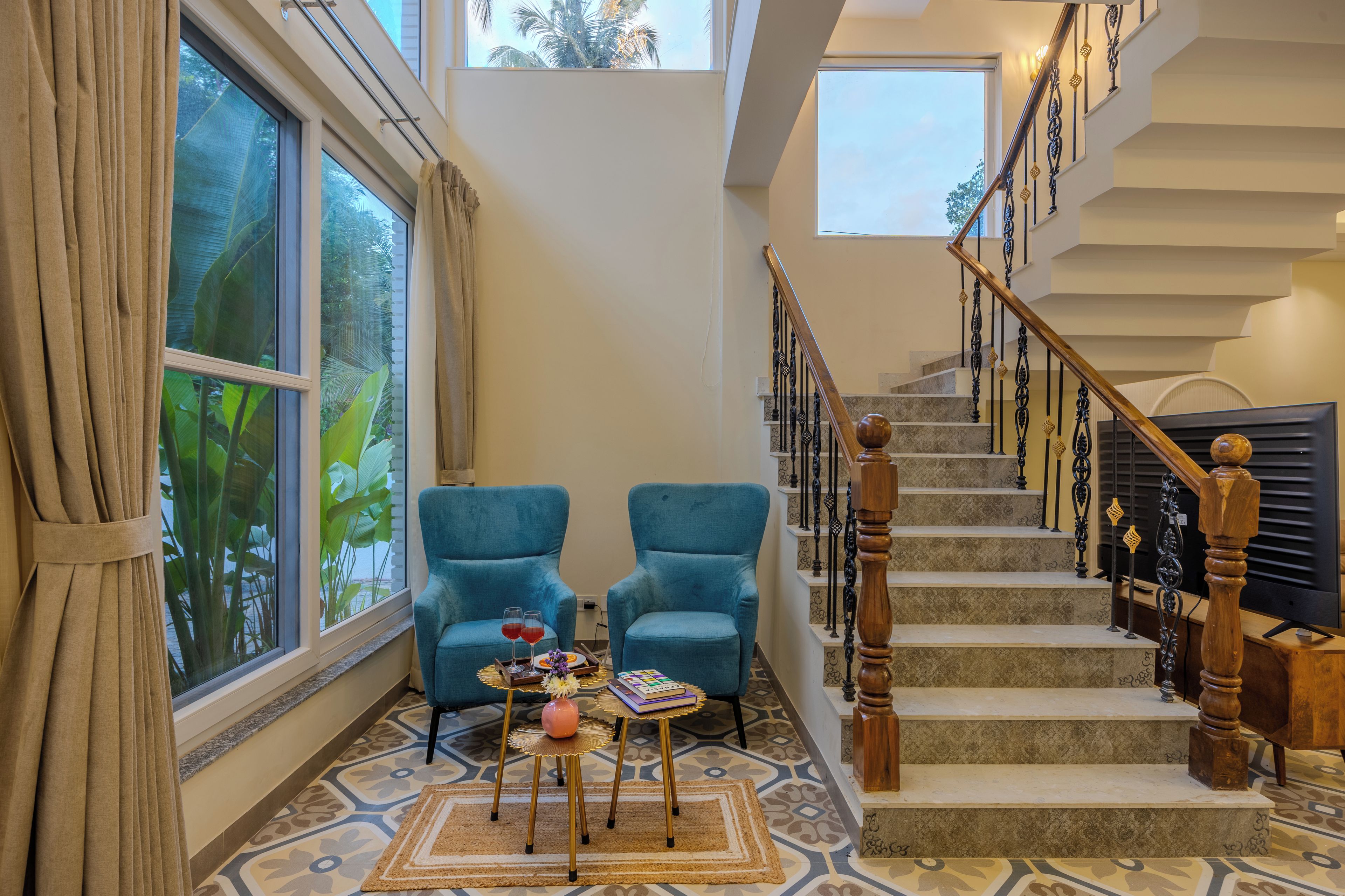 A spacious living area with a large window, a staircase with ornate railings, and two blue armchairs.