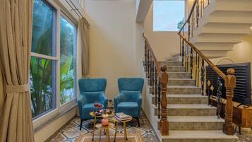 A spacious living area with a large window, a staircase with ornate railings, and two blue armchairs.