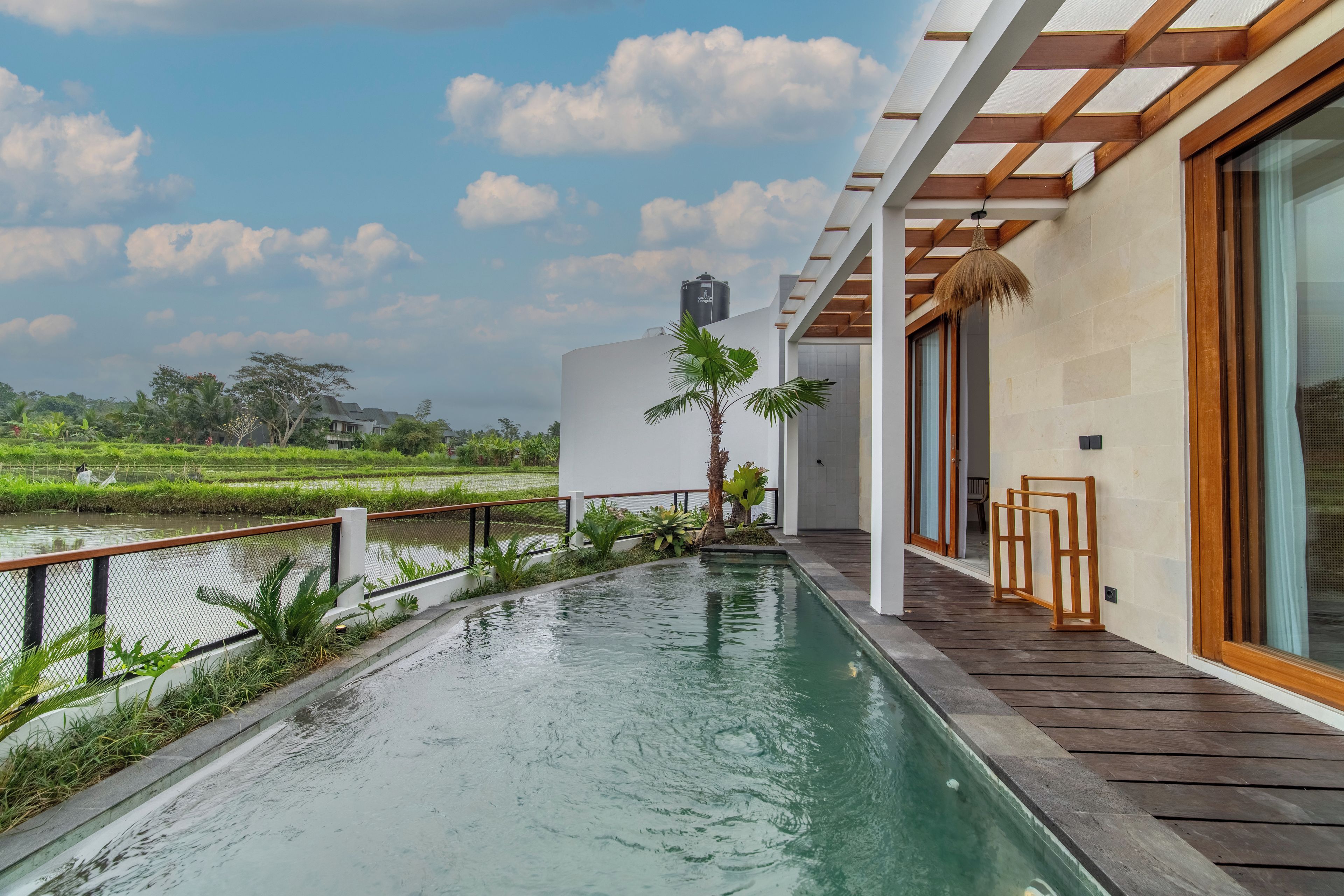 Un edificio moderno con piscina, terraza de madera y vistas a un campo de arroz.