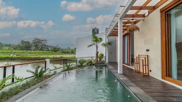 Un edificio moderno con piscina, terraza de madera y vistas a un campo de arroz.