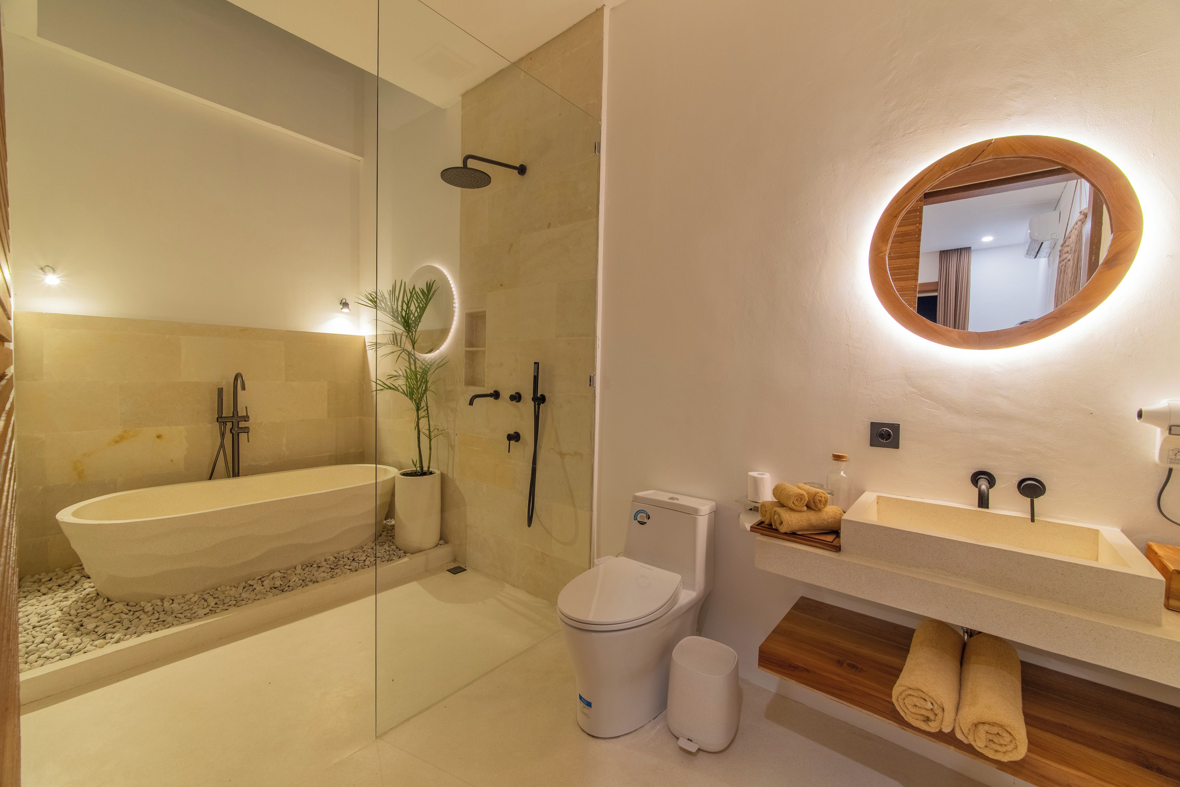 A modern bathroom with a freestanding bathtub, a toilet, a sink with a wooden vanity, and a mirror with a wooden frame.