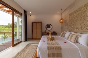 A bedroom with a large bed, a wooden wardrobe, a mirror, and a view of a water body. - SagaLuna Private Villa (gianyar)
