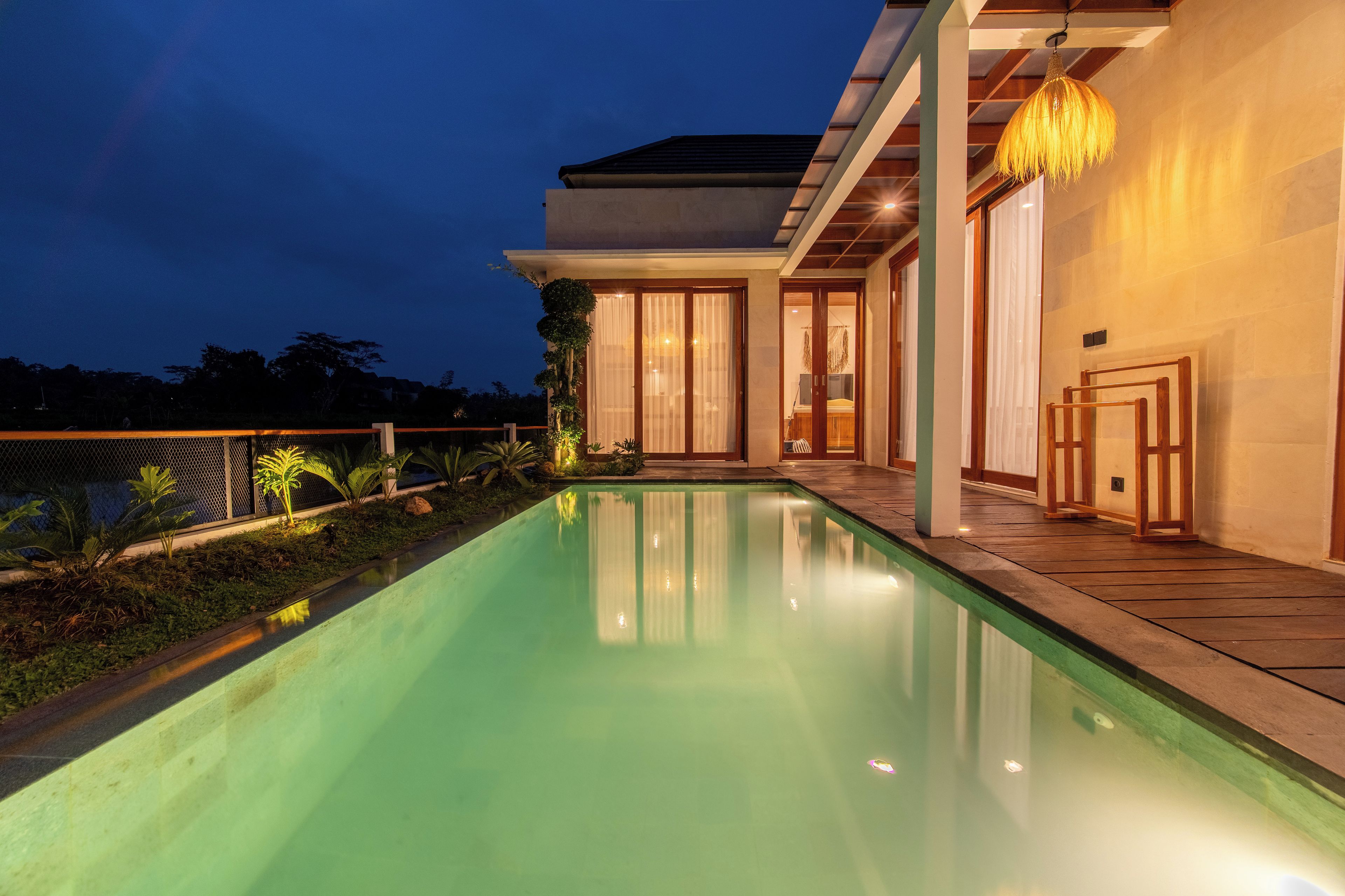 A modern house with a swimming pool, large windows, and a well-lit interior.