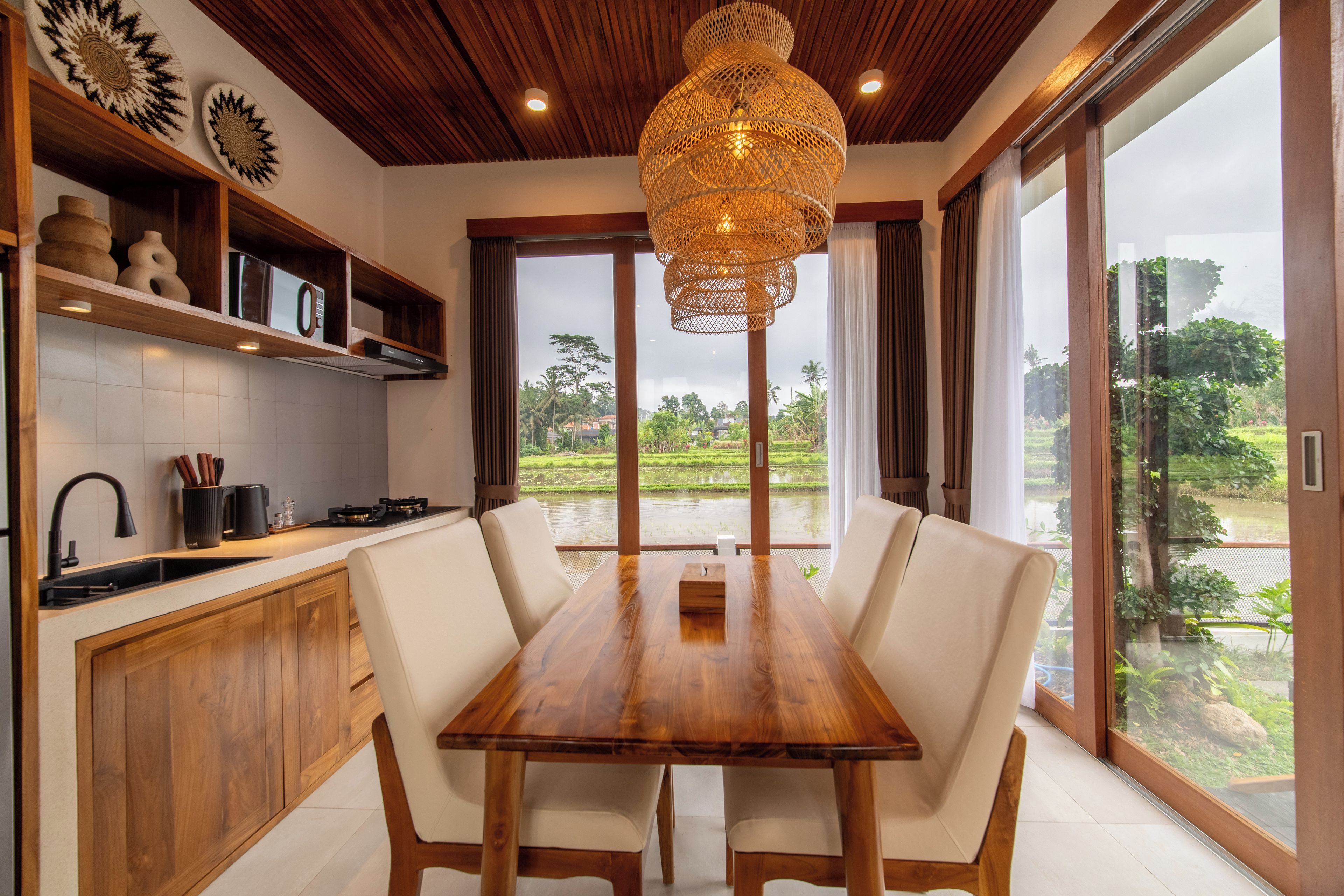 A modern kitchen with a dining area, wooden ceiling, and large windows.
