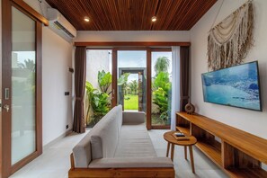A modern living room with a sofa, a wooden coffee table, and a flat-screen TV mounted on the wall. - SagaLuna Private Villa (gianyar)