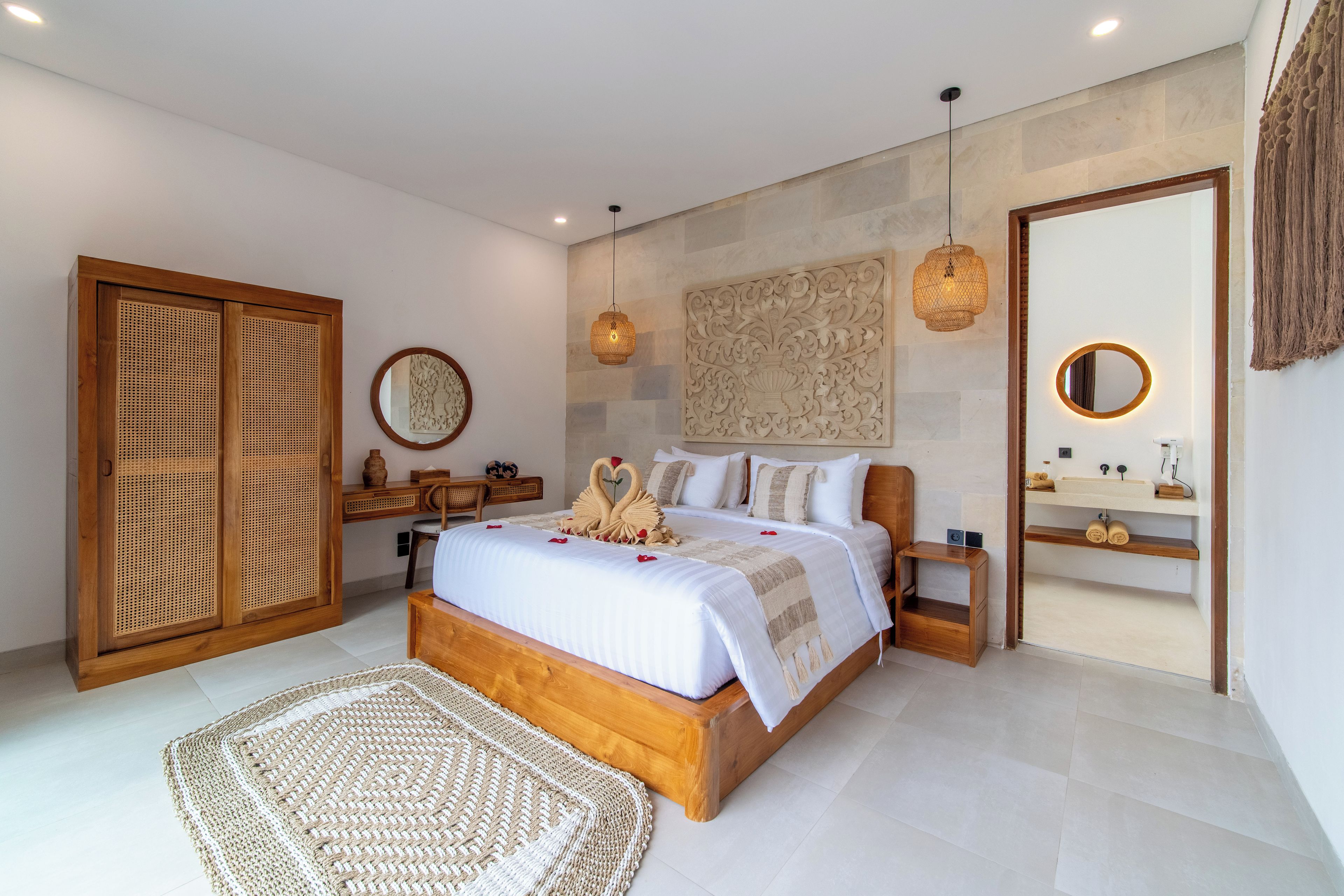 A modern bedroom with a wooden bed, a rattan wardrobe, a desk, and a bathroom with a mirror and sink.