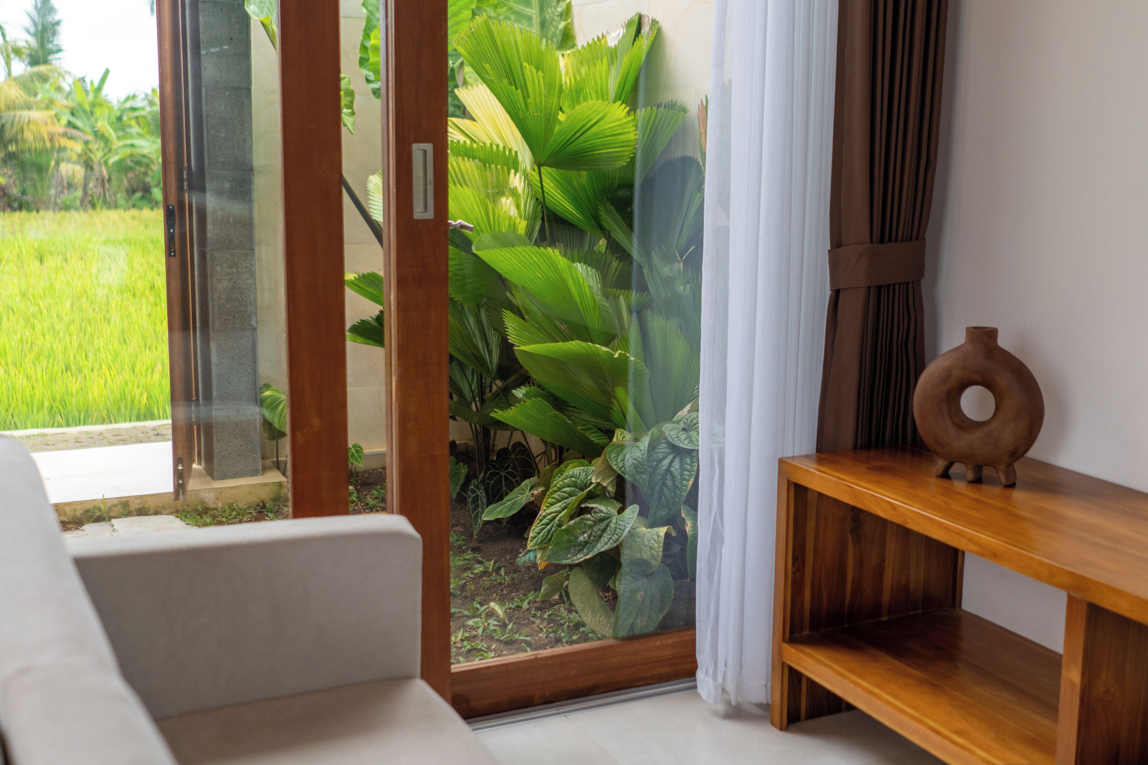 A room with a sliding glass door leading to a garden, a wooden console table, and a white sofa.