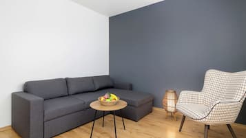 A modern living room with a grey sofa, a round wooden coffee table with fruit, a checkered armchair, and a dark blue accent wall.