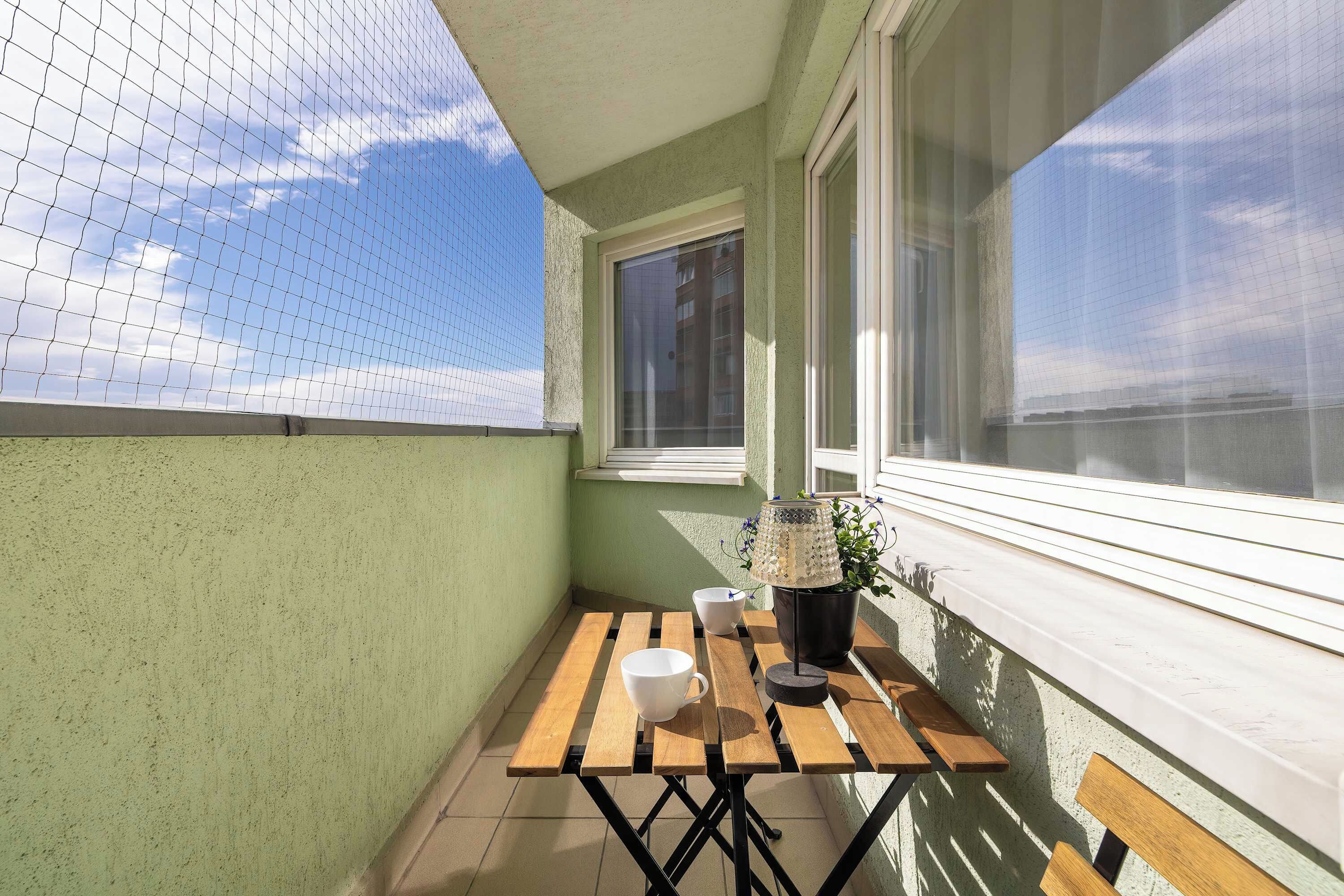 Un balcon avec une table en bois, une plante en pot et une fenêtre.