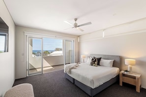 A hotel room with a bed, a nightstand, a lamp, a ceiling fan, and a view of the sea through large windows. - Bayview on Smith—Poolside Sanctuary & Ocean Vistas (Dunsborough)