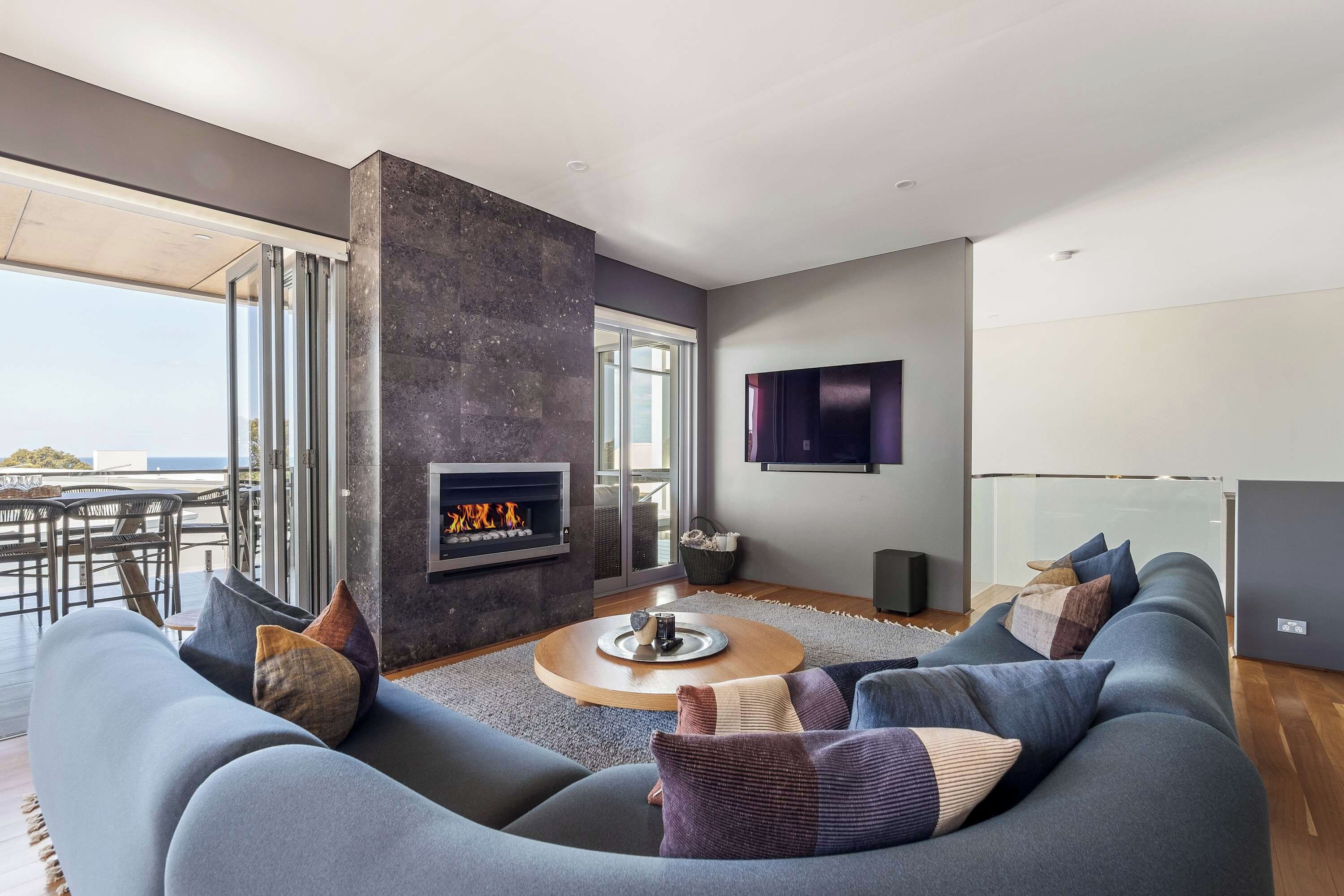 A modern living room with a fireplace, a large sofa set, and a television mounted on the wall.