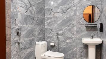A bathroom with a shower, toilet, and sink, all against a marble wall.