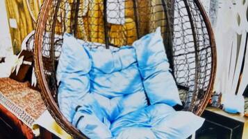 Una silla colgante con cojines azules en una habitación con pared estampada y una mesa de vidrio.