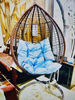Una silla colgante con cojines azules en una habitación con pared estampada y una mesa de vidrio.
