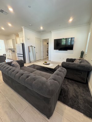 Ein modernes Wohnzimmer mit einem dunkelgrauen Ecksofa, einem Couchtisch und einem an der Wand befestigten Flachbildfernseher.