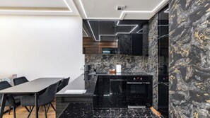 Cozinha moderna com bancadas pretas, forno embutido e painel de fundo em mármore.