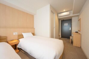 Et hotelværelse med to senge, et skrivebord og en dør til et badeværelse.