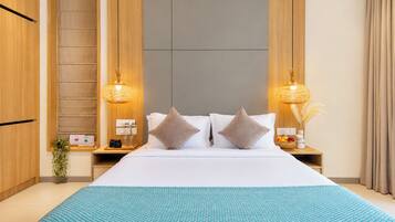 A hotel room with a large bed, two bedside lamps, a nightstand with a fruit bowl, and a wooden wardrobe.