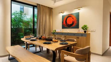 Un espace de repas moderne avec une table en bois dressée pour quatre personnes, un banc et une vue sur la verdure à l’extérieur.